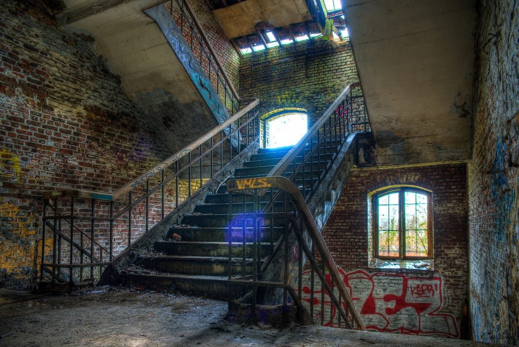 Cage d'escalier éclairée par une fenêtre, murs couverts de graffitis